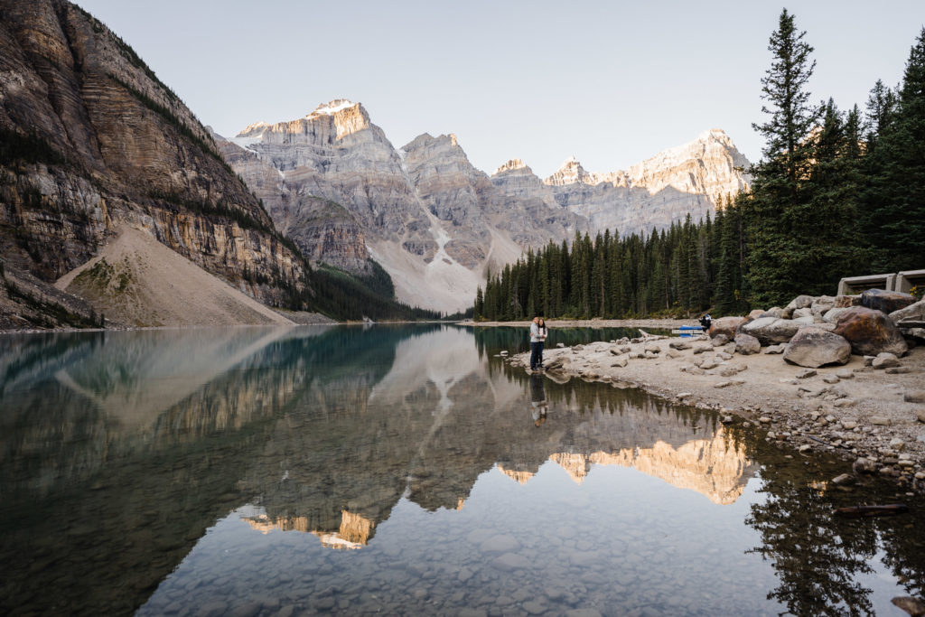 Couple embraces while the mountains reflect in Moraine Lake