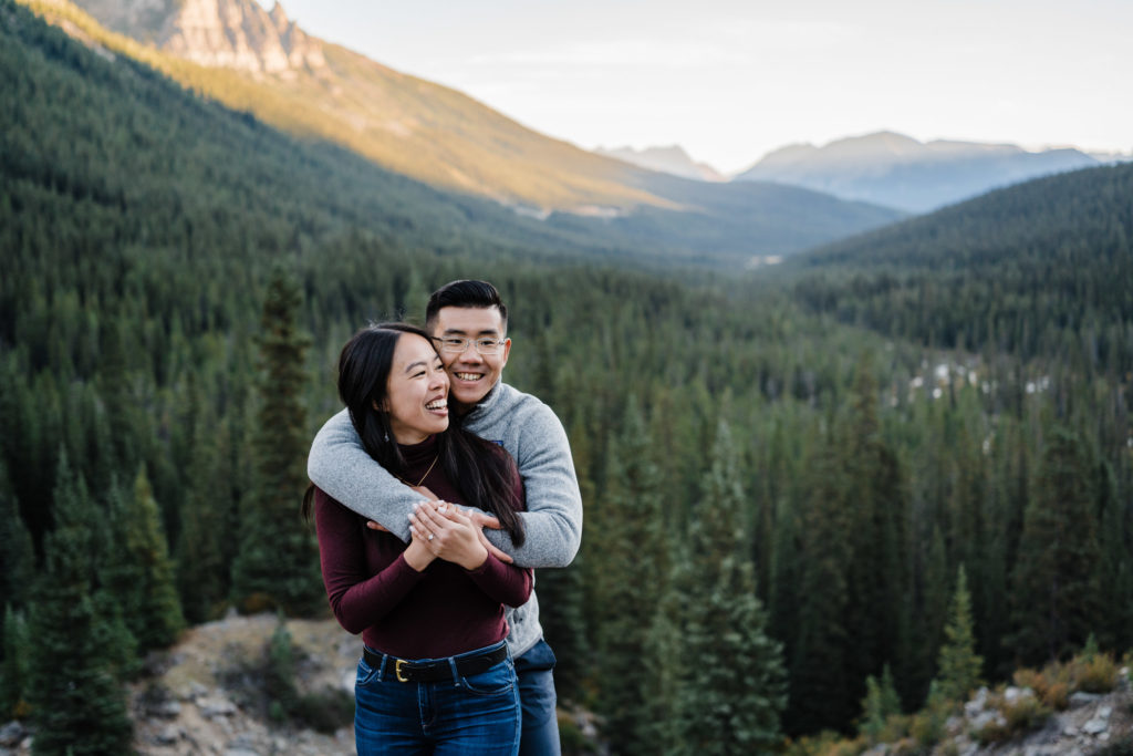 Couple hugs as the sun lights up the valley behind them in Banff
