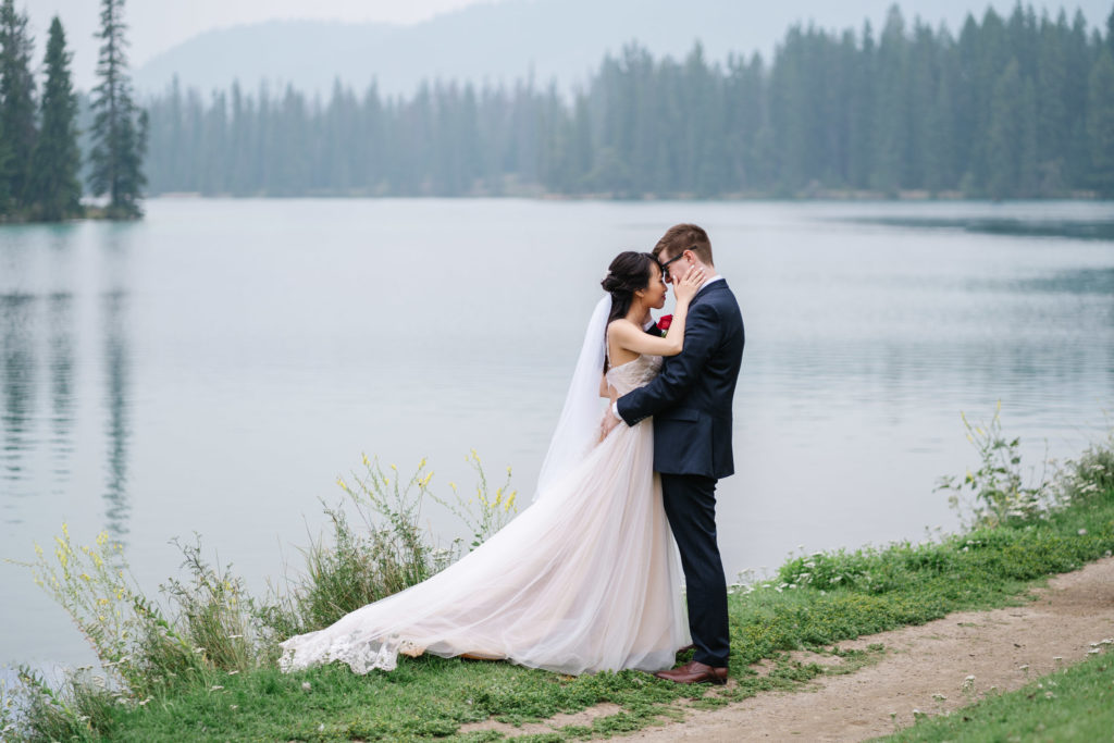Bridge and groom embrace on shores at the Jasper Park Lodge