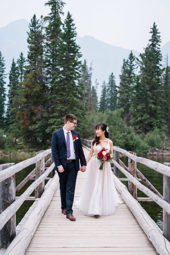 Bride and groom walk hand in hand on bride at Pyramid Island in Jasper National Park