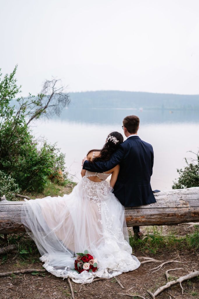 Bride and groom sit on log and look out at Pyramid Lake together