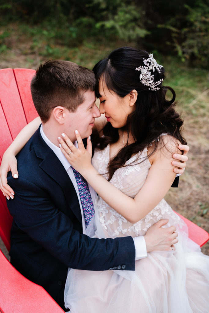 Bride sits on grooms lap in a red chair in Jasper National Park