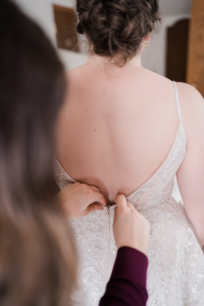 A brides sister does up her wedding dress. 