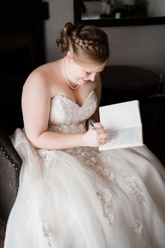A bride sits in her wedding dress while finishing up writing in her vow book. 