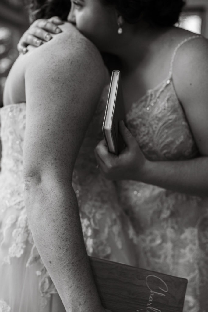 Brides embrace while holding vow books after vow exchange. 