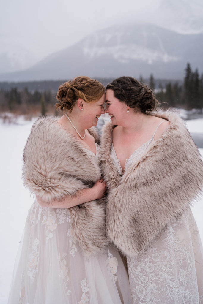 Two brides press their foreheads together during a cold winter wedding in Canmore. 