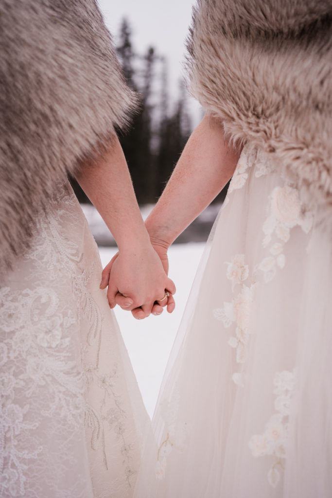 Close up of two brides hands, wedding dresses, and fur shawls in winter wedding. 