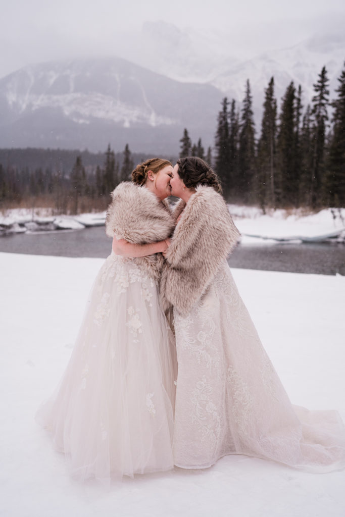 Two brides kiss during winter wedding in Canmore. 
