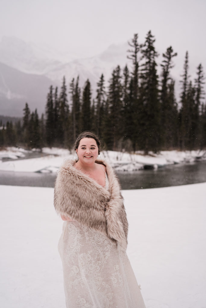 Bride wrapped in fur shawl looks off to the mountains. 
