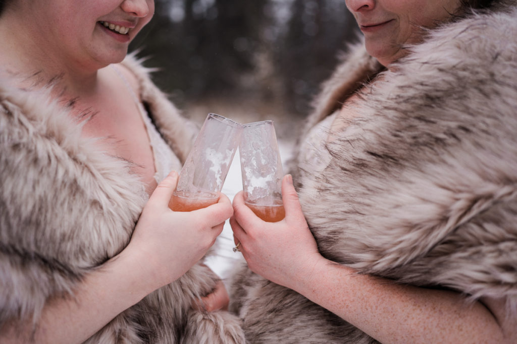 Brides cheers frozen glasses of champagne during winter wedding in Canmore. 