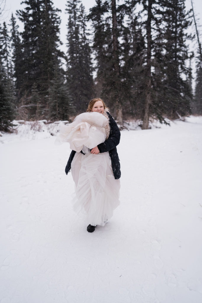 Bride walks in the snow while holding up her dress in Alberta.