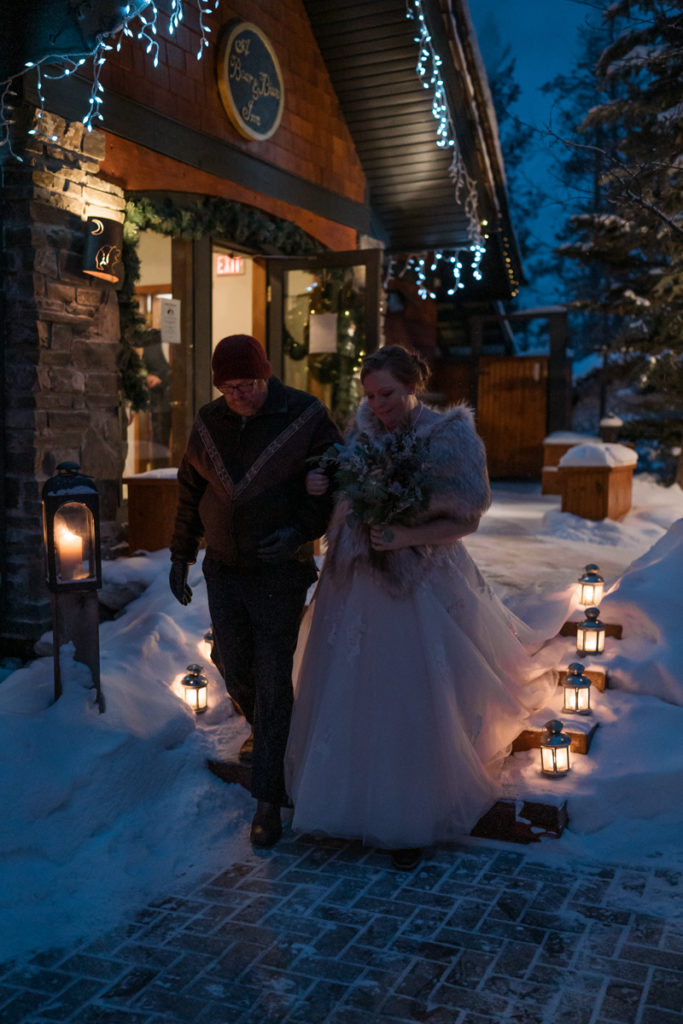 Bride walks down lantern lit aisle for winter sunset wedding. 