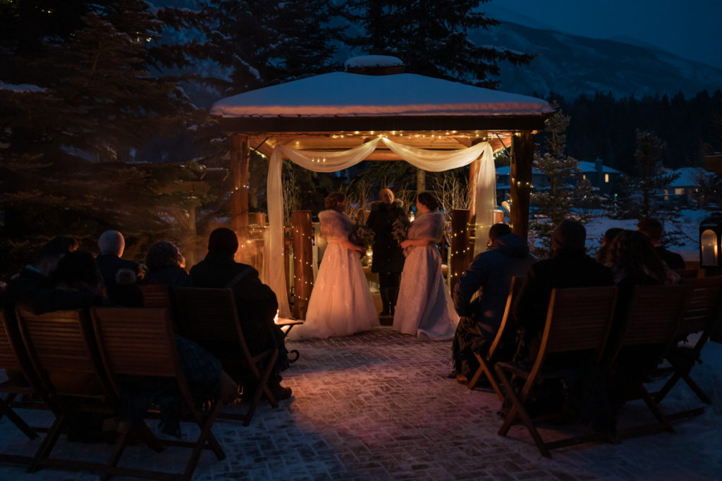 Two brides stand together in outdoor candle lit ceremony in Alberta