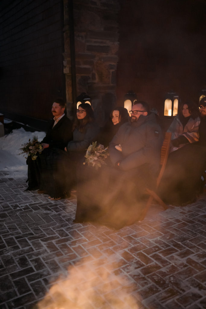 The guests cuddle under customized blankets in outdoor winter ceremony. 
