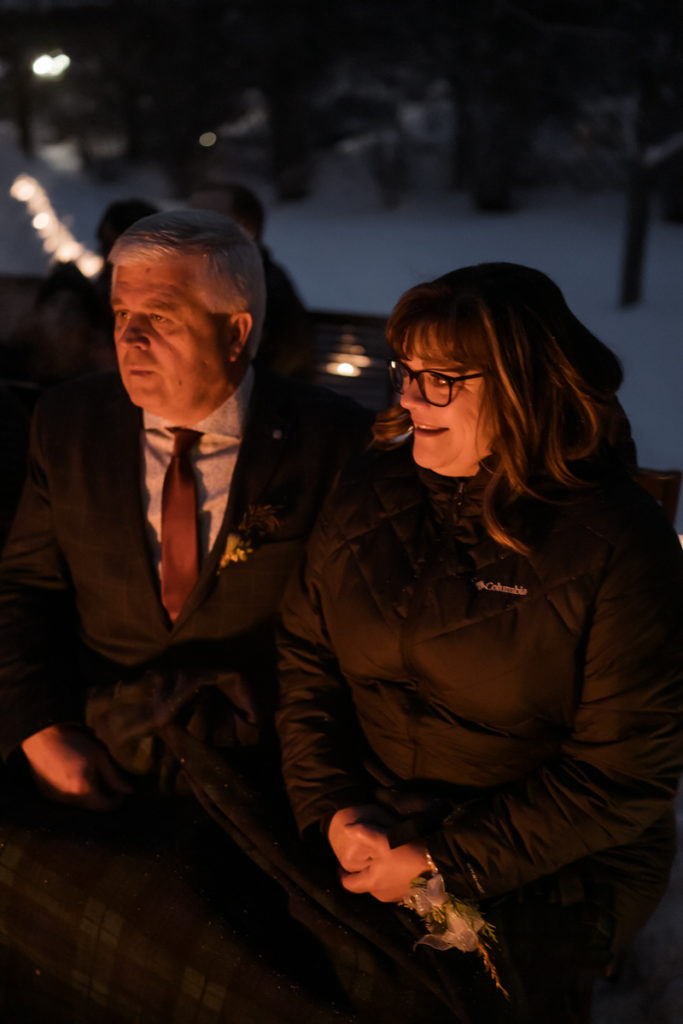 brides parents faces lit up by campfire in outdoor winter ceremony. 