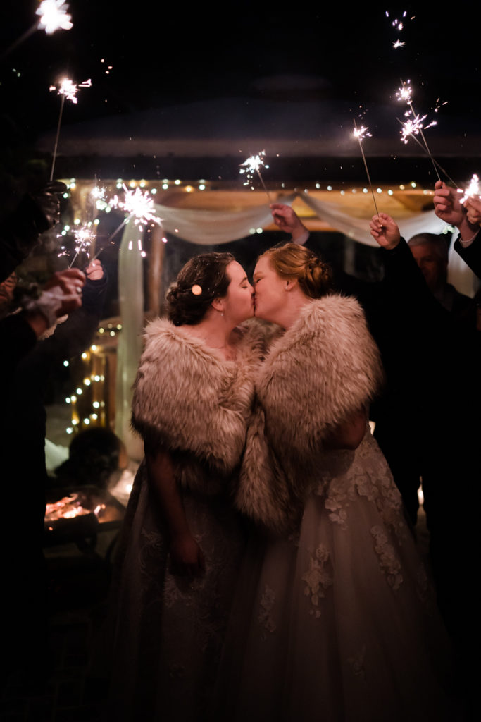 Two brides kiss under sparklers at a wedding at Bear and Bison Inn in Canmore