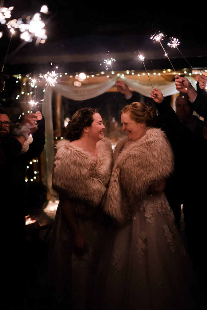 Two brides smile at each other during sparkler exit