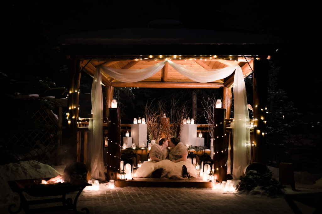 Two brides kiss in gazebo filled with twinkly lights and lanterns at A Bear and Bison Inn