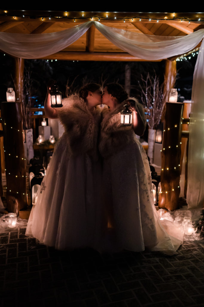 Two brides hold up lanterns in the dark after outdoor winter wedding in Canmore