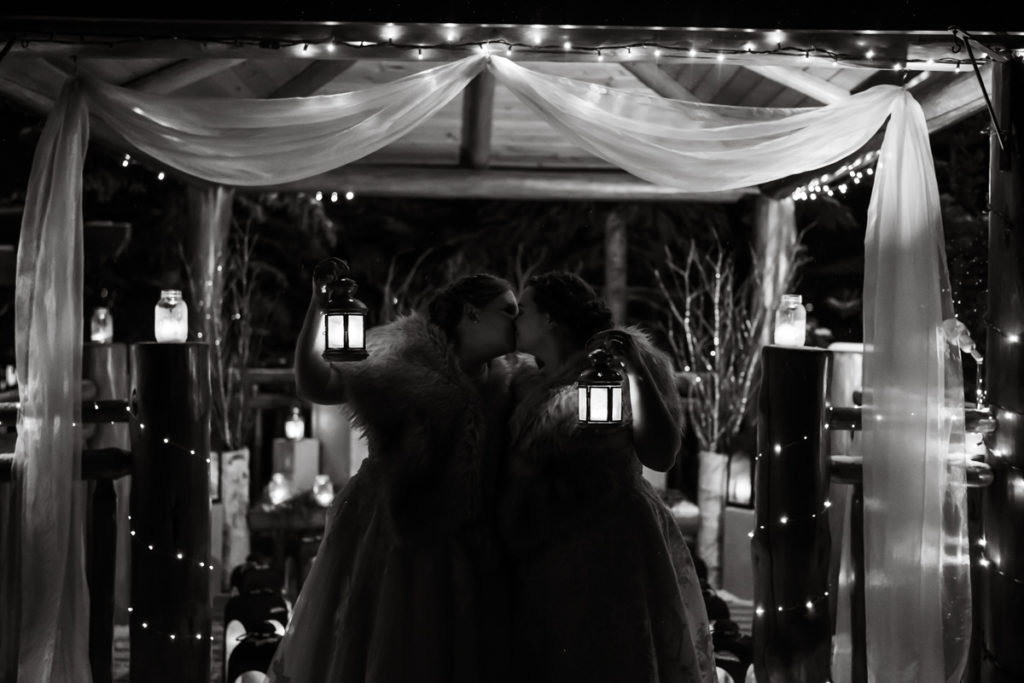 Black and white photo of two brides holding up lanterns surrounded by. twinkling lights