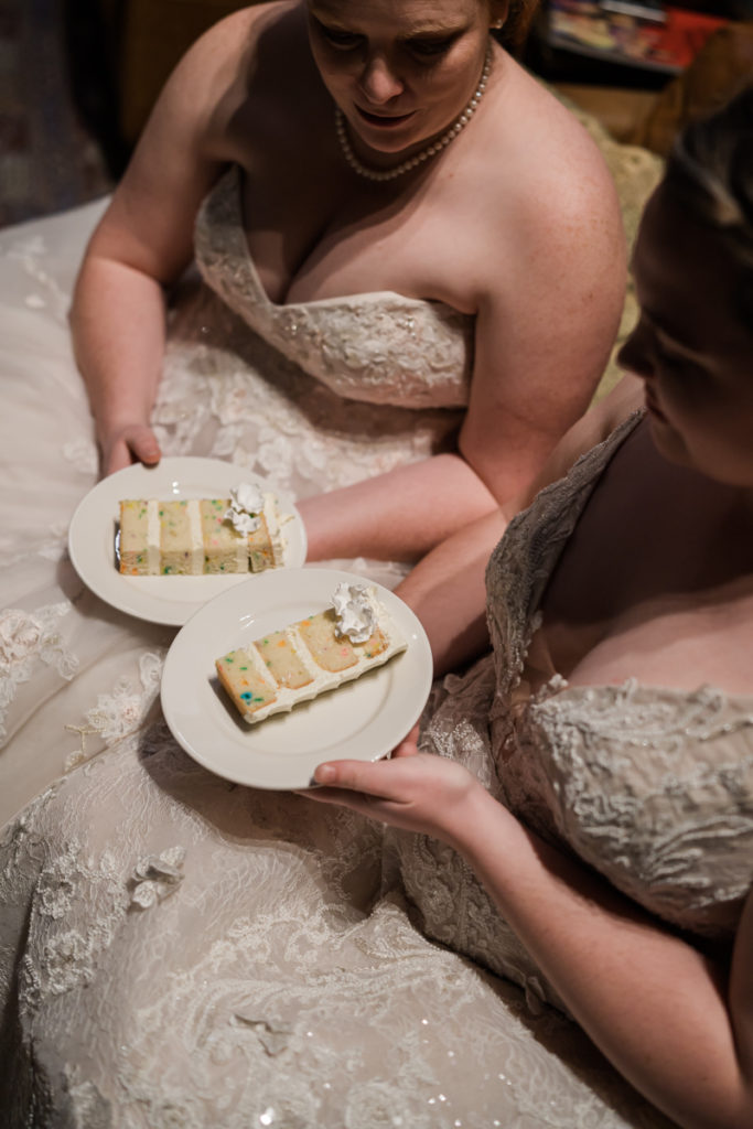 Two brides sit with funfetti cake to celebrate their pride wedding