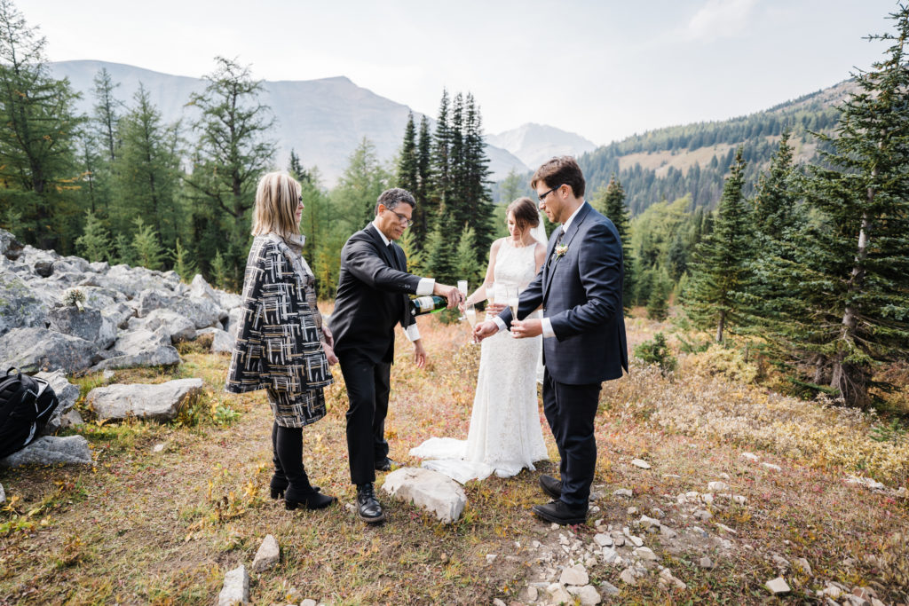 Grooms father pours celebratory champagne after wedding ceremony in the mountains. 