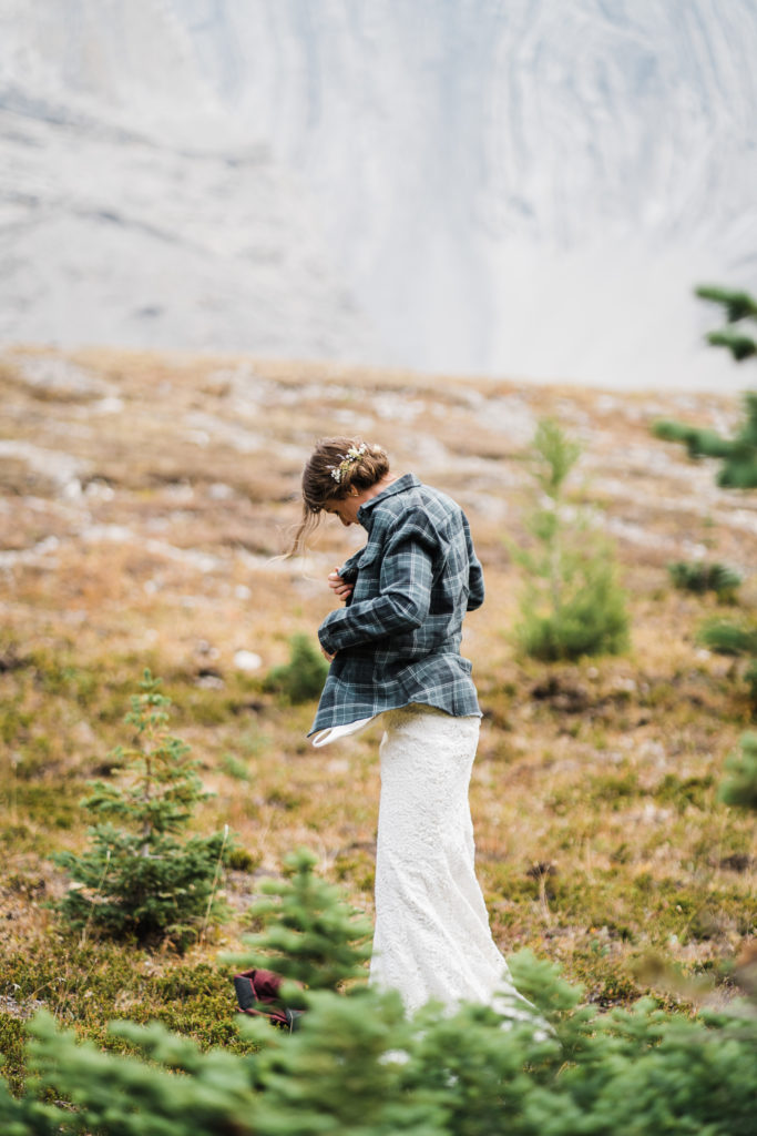 Bride changes into her wedding dress in the sub alpine while wearing a flannel top. 