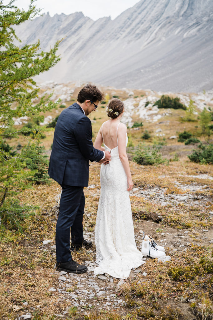 Groom zips up brides wedding dress during their hiking elopement in Kananaskis. 