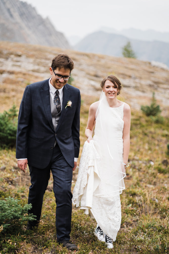 Bride looks at camera while walking with groom during hiking elopement in Kananaskis. 