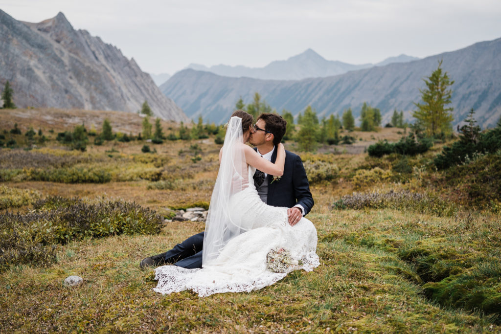 Bride sits on grooms lap in sub alpine meadow during their hiking elopement in Kananaskis. 