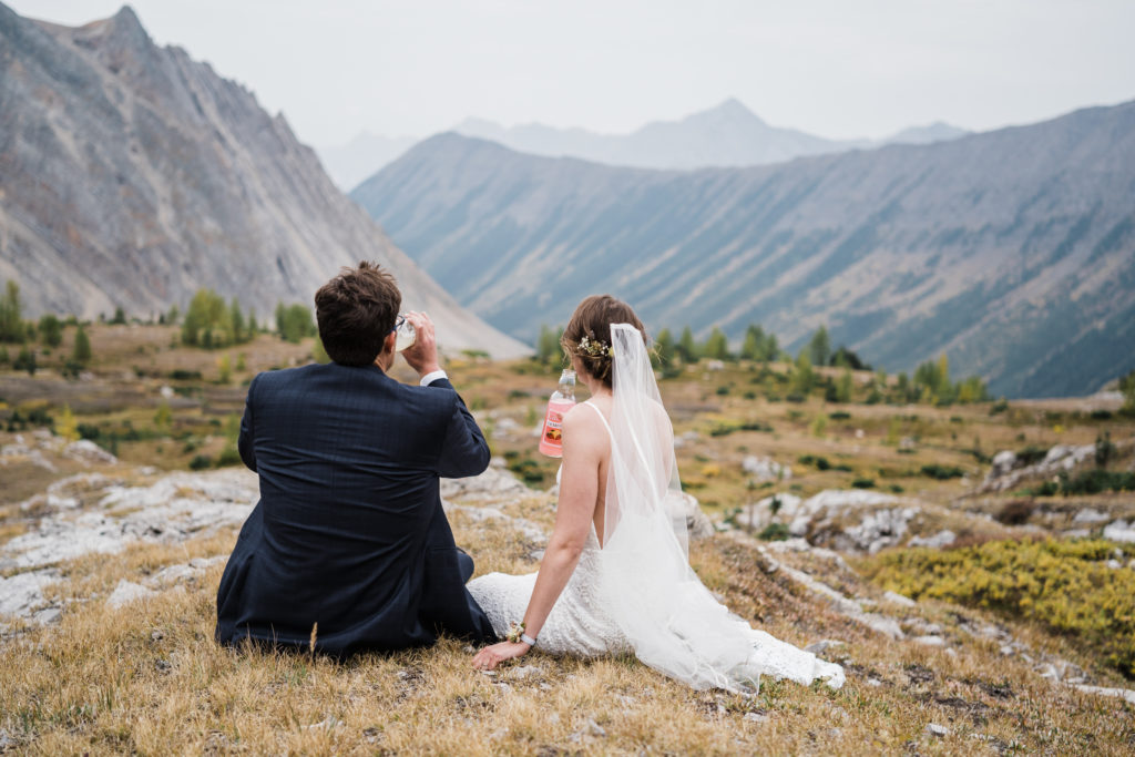 Bride and groom take a break and have some lemonade while sitting in a meadow in the mountains. 