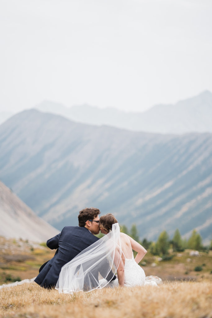 Bride and groom kiss while veil blows in the wind in Kananaskis. 