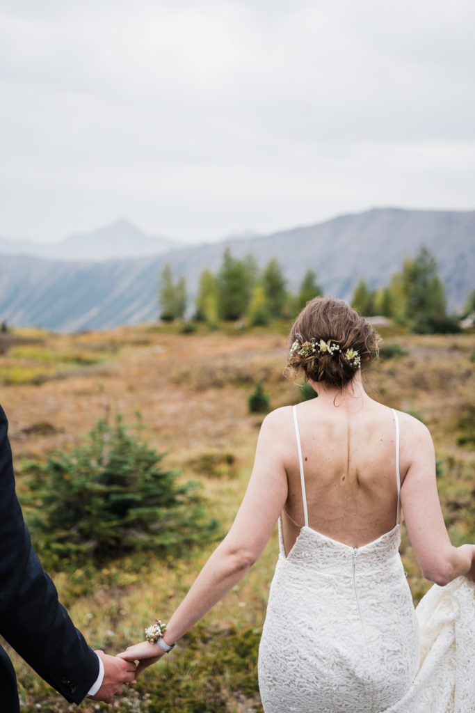 Back of the brides head while the groom holds her hand off frame while hiking in Kananaskis. 