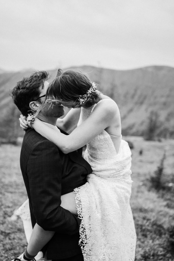 Black and white photo of groom holding bride up and them kissing. 