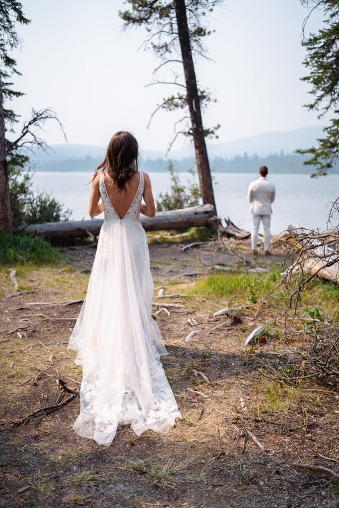 A bride walks towards the turned around groom before their first look in Jasper National Park.
