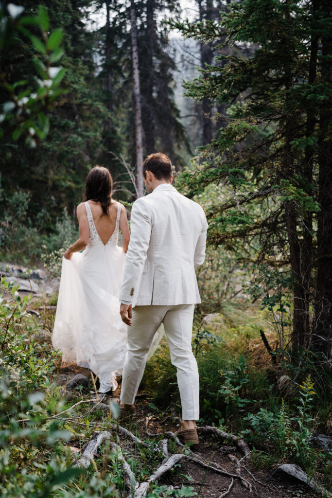 Bride leading the way down a forested pathway while the groom follows close behind.