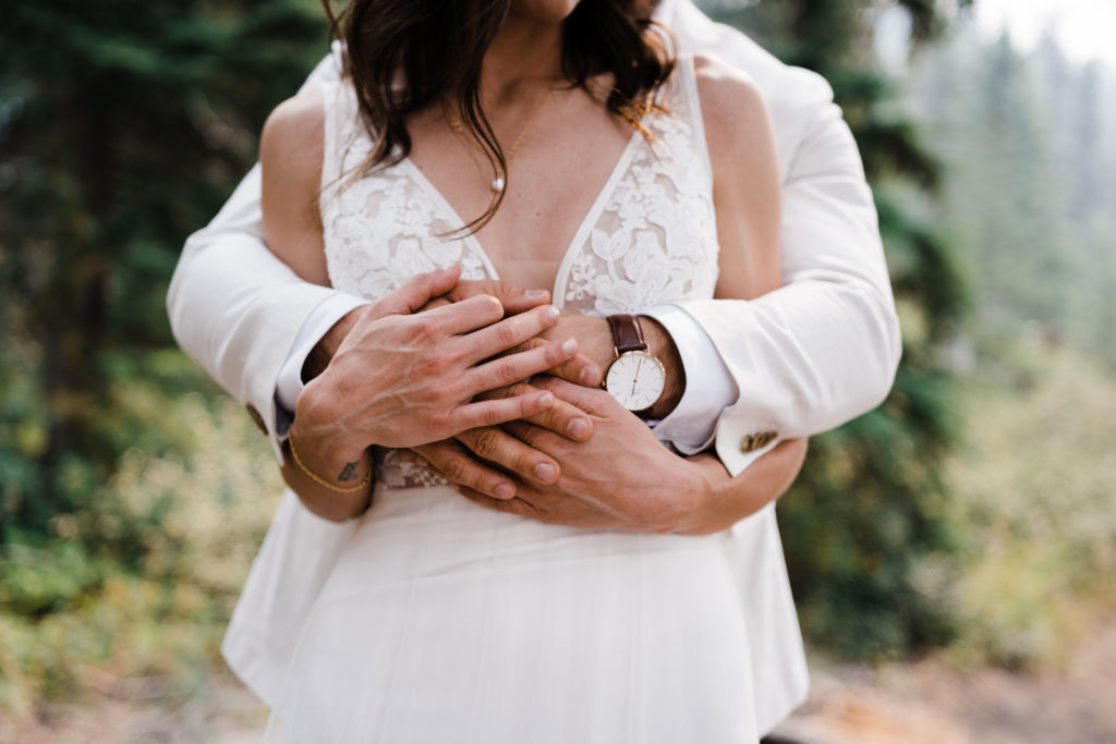 Detail photo of groom holding bride from behind with their hands embraced.