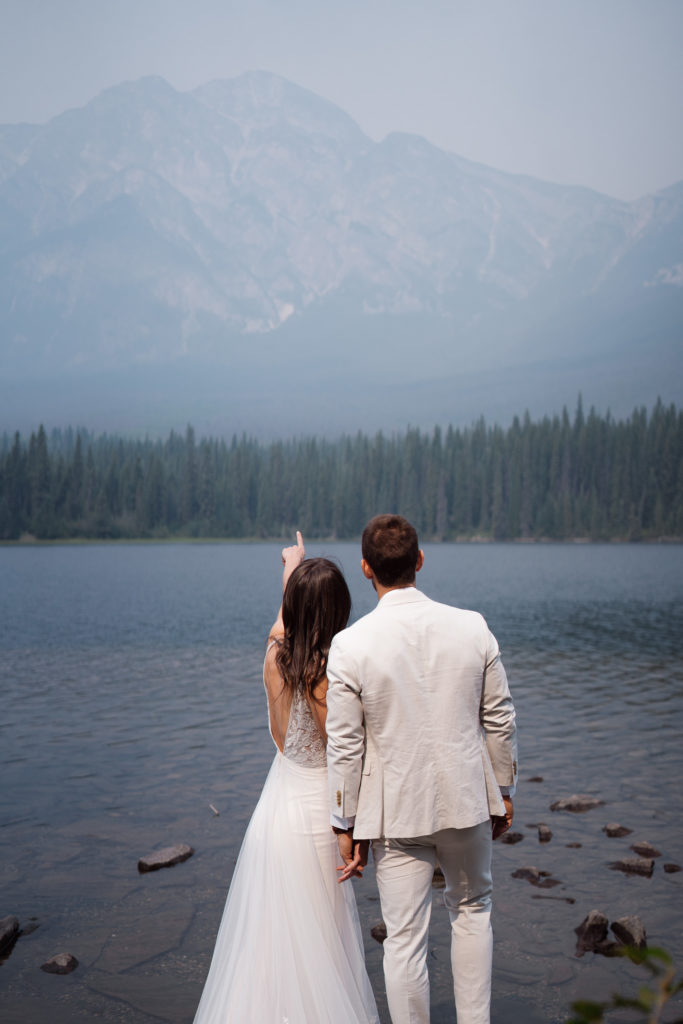 Bride and groom hold hands while bride points up at Pyramid Mountain in Jasper National Park