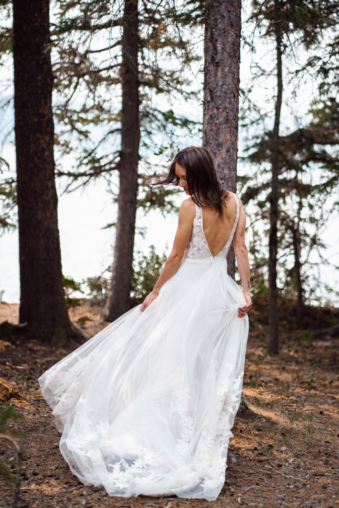 Bride twirls in lace dress in forest in Jasper National Park. 