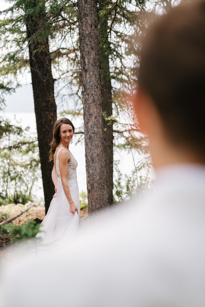 Bride stands infront of groom looking at him while photograph is taken over his shoulder in Jasper National Park.