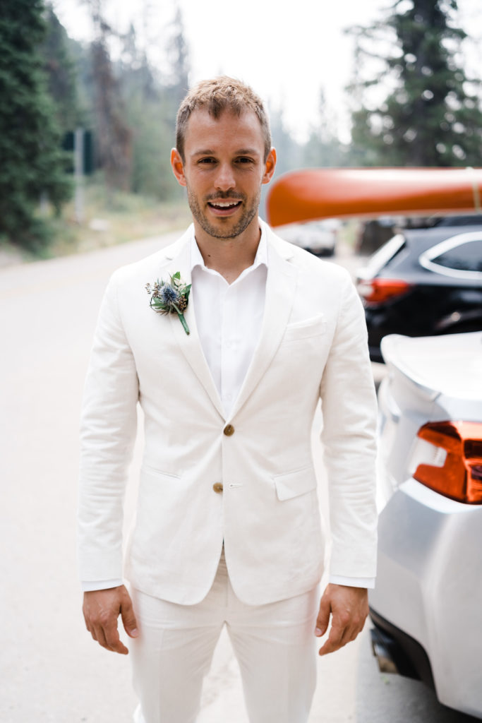 Groom stands in parking lot at Pyramid Island in a white suit. 