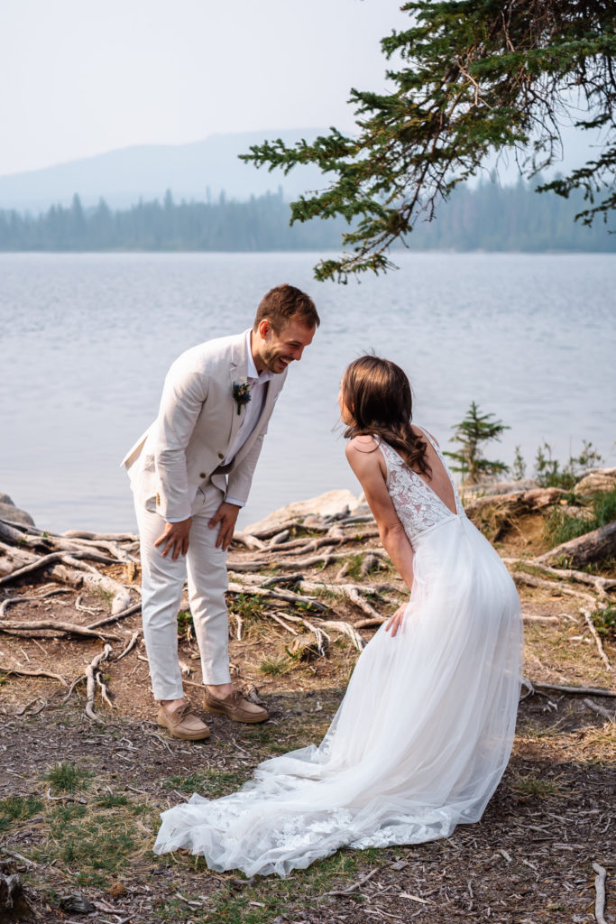 Bride and groom face each other and laugh with hands on their knees after their first look in Jasper National Park. 