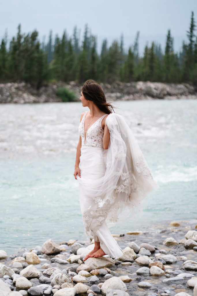 Jasper intimate wedding photographer photo of barefoot bride in lace dress at the Snaring river in Jasper National Park. 