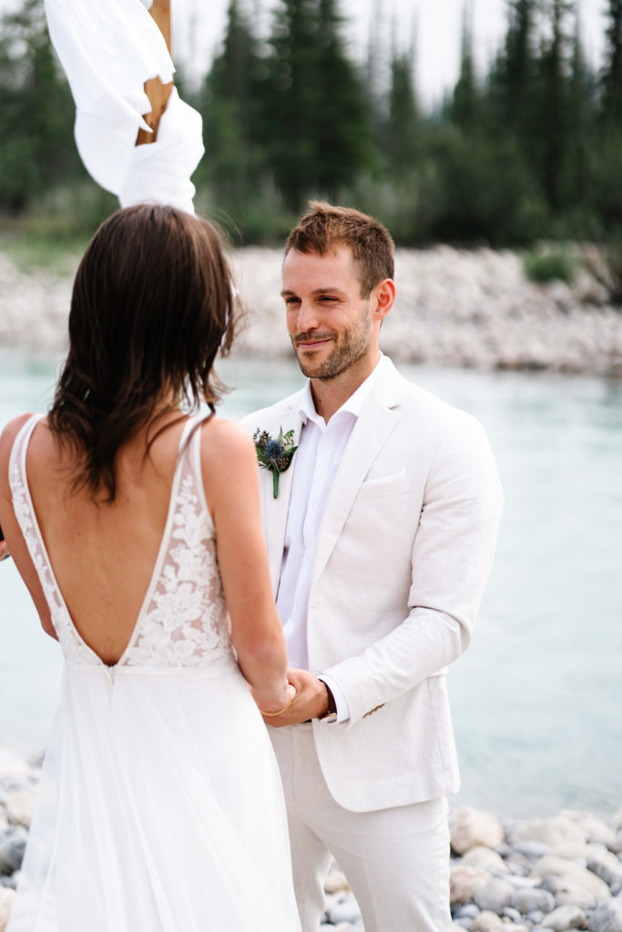 groom looks at bride while holding her hands during intimate ceremony in Jasper National Park. 