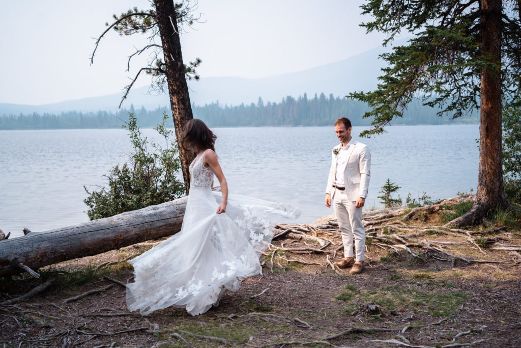 Bride twirling in her flowing wedding dress while groom looks towards her at Pyramid Island in Jasper National Park.