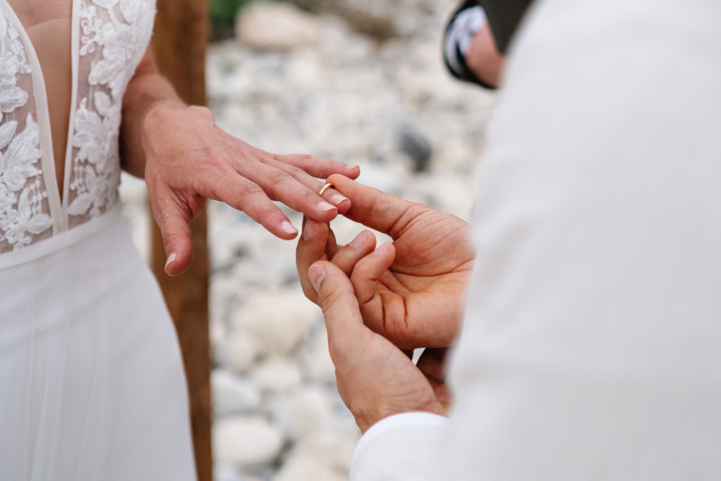 close up of groom sliding ring on brides finger in intimate wedding ceremony at the Snaring River.