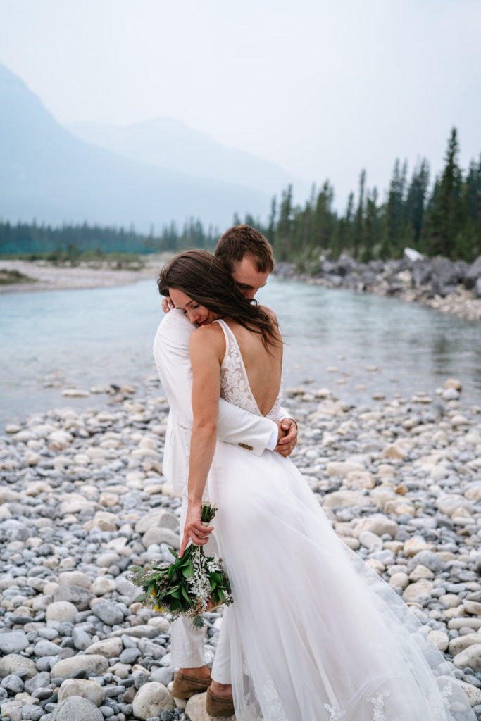Bride and groom embrace next to the snaring river.