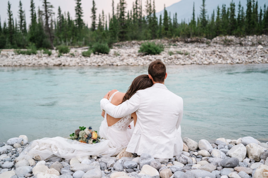 Jasper intimate wedding photographer captures quiet moment of bride and groom sitting next to snaring river.