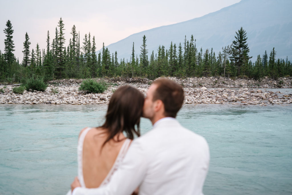 bride and groom in foreground out of focus with the mountains of Jasper National Park in the background.