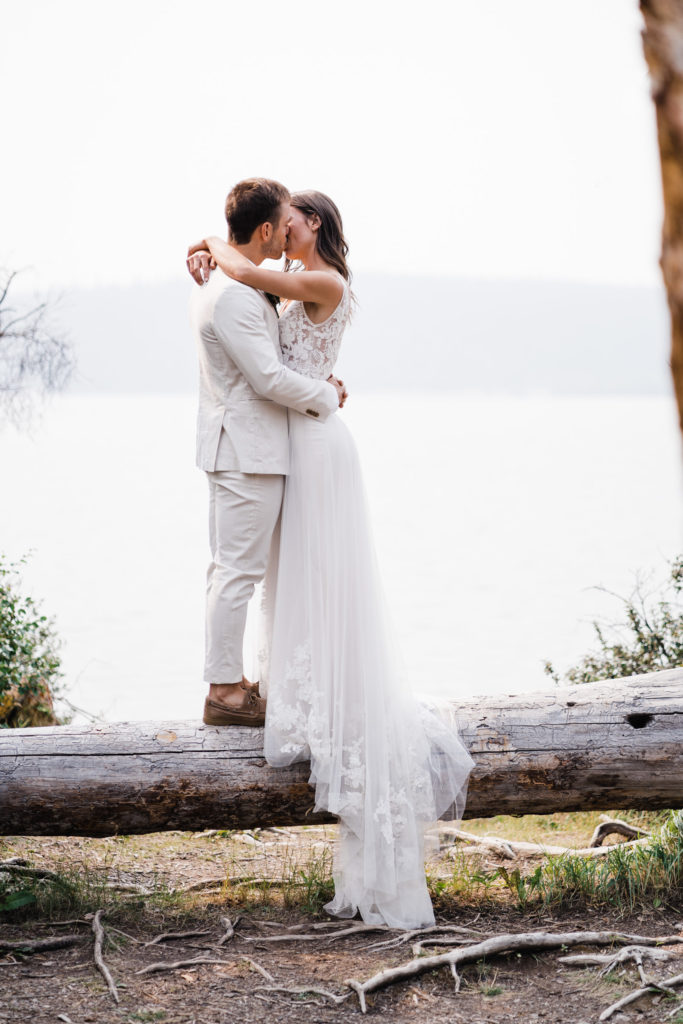 Bride and groom kissing while standing on a log at Pyramid Island in Jasper National Park.